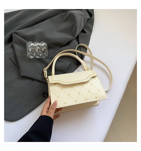 Detail of cream crossbody bag featuring quilted heart embroidery and gold hardware