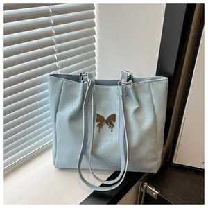 Détail du sac cabas bleu clair avec texture craquelée et breloque papillon en métal