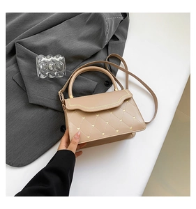 Close-up of beige quilted crossbody bag with gold heart studs and wavy flap detail