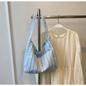 Detail of colorful striped nylon shoulder bag hanging on a rack with cream dress background