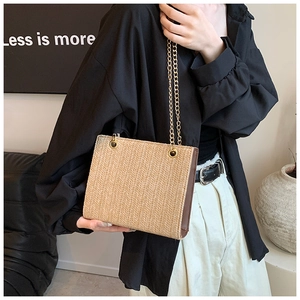 Detail of woven straw tote bag with golden chain strap and brown leather side panel