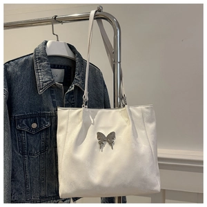 Détail du sac cabas blanc avec breloque papillon argentée sur une veste en jean