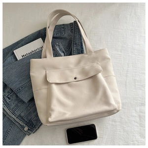 Détail d'un sac cabas en toile crème avec poche frontale et fermeture par boucle en métal