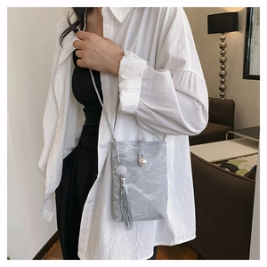 Detail of light gray crossbody bag with paper texture, pearl button and tassel fringe