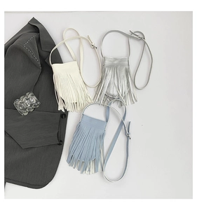 Flat lay of tassel crossbody mini bags in white, silver, and blue with adjustable straps
