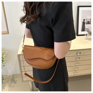 Brown leather saddle bag with wavy flap shown on a model in a minimalist home setting