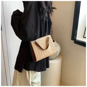 Detail of woven straw tote bag with brown leather trim and golden metal rings