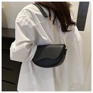 Detailed view of black saddle bag with wavy leather texture and gold chain strap