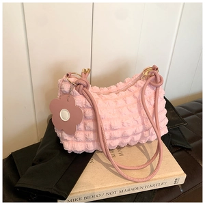 Detail view of pink bubble textured shoulder bag with a floral charm on white wood