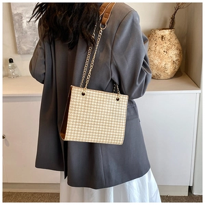 Detail of woven houndstooth tote bag with gold chain strap on grey blazer model