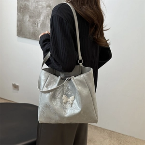 Grand sac cabas argenté avec détail papillon porté à l'épaule par un mannequin de profil