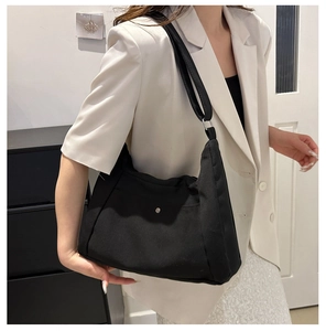 Detail showing black canvas shoulder bag with silver buckle and adjustable strap on a person