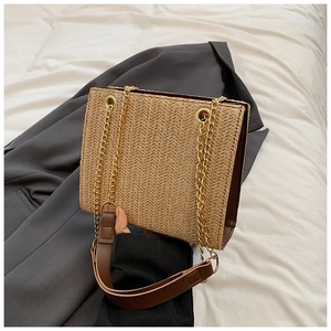 Detail of woven straw tote bag with brown leather handles and gold chain straps