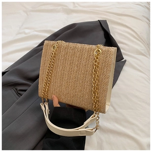 Detail of khaki woven straw tote bag featuring chic gold metal chain and cream leather strap