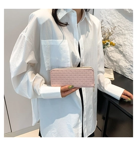Detail of light pink clutch wallet with geometric woven texture held by a model