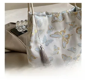 Gros plan sur la broderie papillon dorée et le gland en soie du sac seau beige chic
