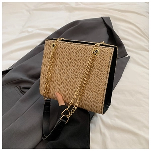 Detailed view of woven straw tote bag with golden chain strap and herringbone pattern