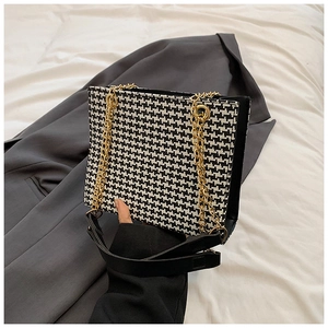 Close-up of houndstooth tote bag featuring gold chain strap and black shoulder strap