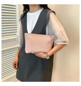 Detail of pink woven texture clutch bag held by model against a minimalist background
