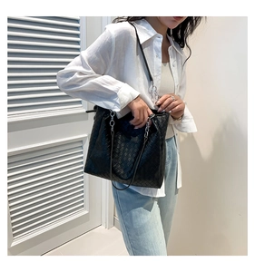 Detail of black woven leather tote bag with silver chain strap worn over the shoulder