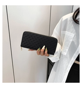 Close-up of black woven long wallet with gold zipper held by hand in a minimalist setting