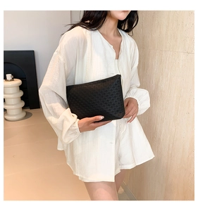 Detail view of a black hollow woven clutch bag held by a model in a minimalist setting