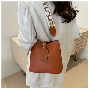 Brown litchi grain bucket bag with wide patterned strap shown on a white blazer