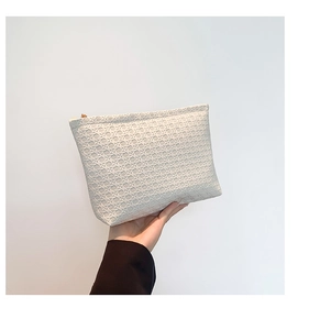 Close-up of white woven envelope clutch with golden zipper detail held by hand