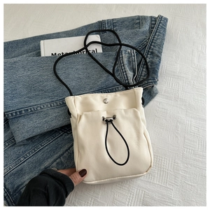 Détail du sac à bandoulière en toile crème avec cordon noir et bouton pression métallique