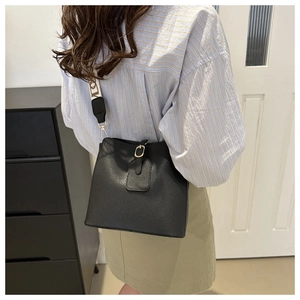 Detail of black pebbled leather bucket bag with wide decorative letter strap and metal buckle
