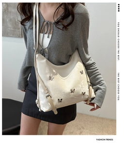 Détail d'un grand sac cabas beige avec des breloques papillon en métal et une texture douce
