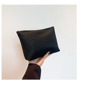Close-up of black woven leather envelope clutch bag held by hand on white background