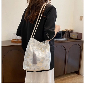 Détail du sac seau crème avec broderie de papillon bleu et long gland décoratif élégant