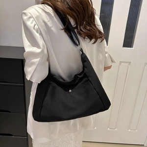 Minimalist black canvas tote bag with silver buckle worn by model in a modern interior