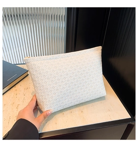 Detail of white woven envelope clutch with golden zipper held against marble background