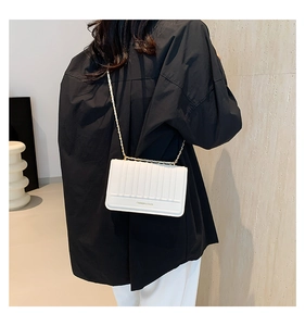 Rear view of a minimalist white quilted chain bag with gold text on a black shirt