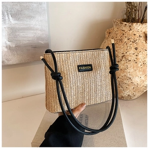 Dettaglio della borsa a spalla in paglia intrecciata con tracolla a nodo e logo fashion