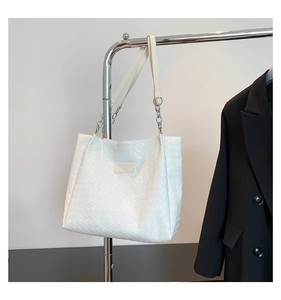 Detail of white woven tote bag with silver chain strap and fashionable leather tag