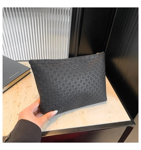 Detail of hand holding a black woven texture clutch bag with golden metal zipper