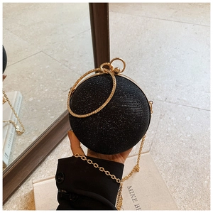 Detail of a black glitter sphere evening bag with golden ring handles and chain strap