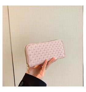 Pink woven long wallet with gold zipper detail held in hand against wood background