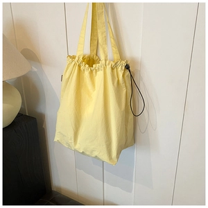 Detail of light yellow nylon tote bag featuring drawstring closure and ruffled edge design