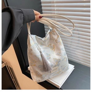 Détail de la broderie papillon élégante et du pompon sur le sac seau blanc chic
