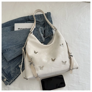 Détail du sac cabas crème avec des clous papillon argentés et une boucle sur le côté