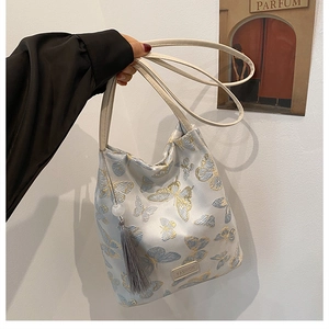 Détail du sac seau brodé avec motifs papillons bleus et pendentif à pampilles grises