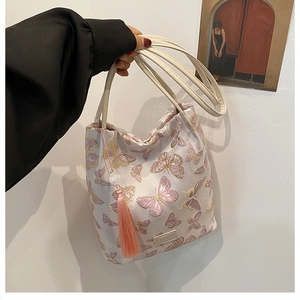 Détail de la broderie papillon et du pompon sur le grand sac seau en toile couleur crème