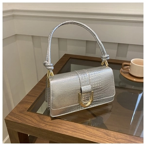 Détail du sac argenté à motif crocodile avec boucle en métal doré en forme de U sur une table