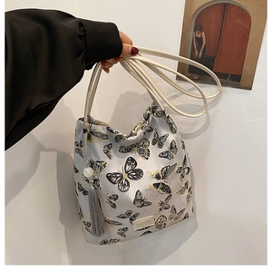 Détail du sac à bandoulière gris clair avec broderie papillon et breloque à pompon