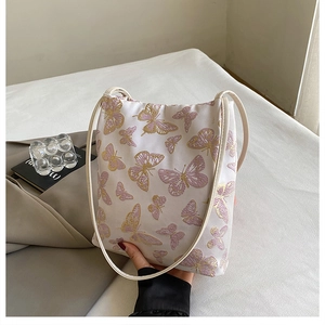 Détail de broderie papillon sur un sac seau beige avec une fine bandoulière