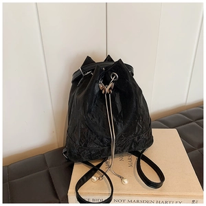 Detail of black pleated drawstring backpack with golden butterfly buckle and pearl accents